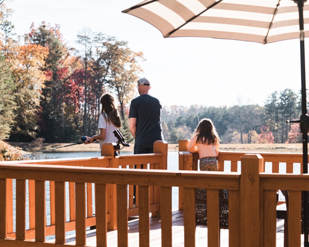 Guests enjoying a peaceful afternoon fishing from the private lakeside deck at Rustic Ruby by Reservable Stays, surrounded by beautiful autumn scenery.